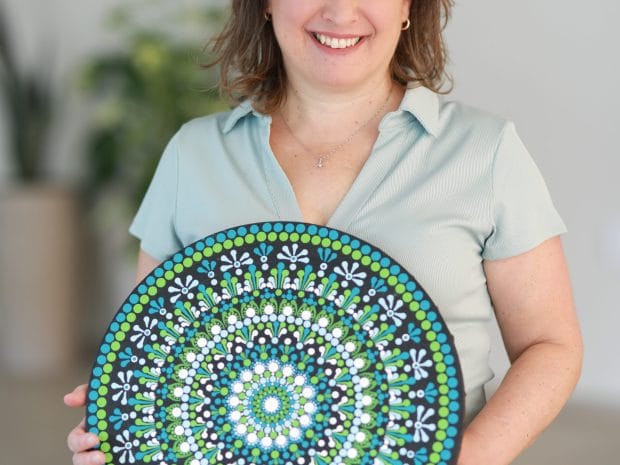 ורד שמיאן מחזיקה צלחת עץ עגולה מעוטרת בציור מנדלה צבעוני