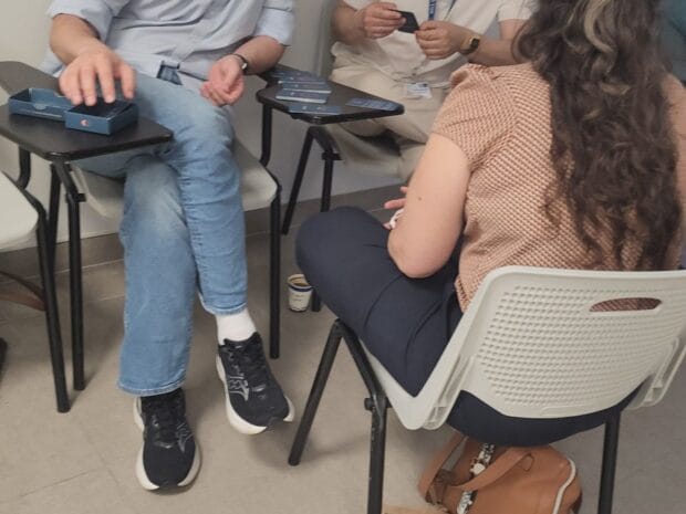 משתתפים יושבים על כיסאות עם קלפים על שולחנות קטנים בסדנה של גיא רמות