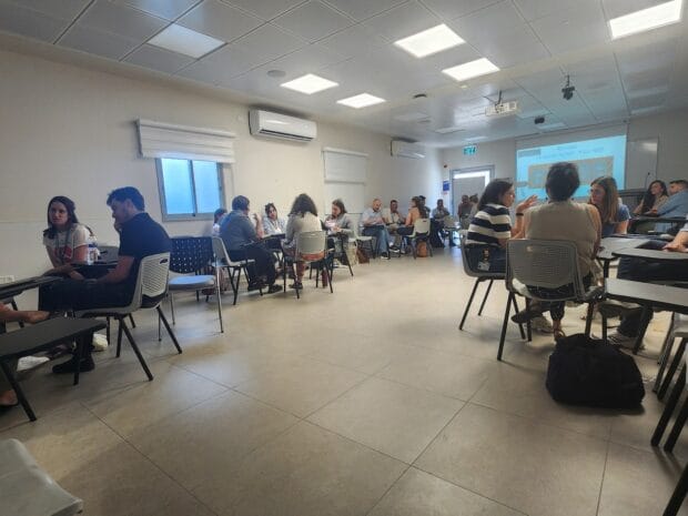 משתתפים יושבים בזוגות בכיתה ומשוחחים במהלך סדנה של גיא רמות